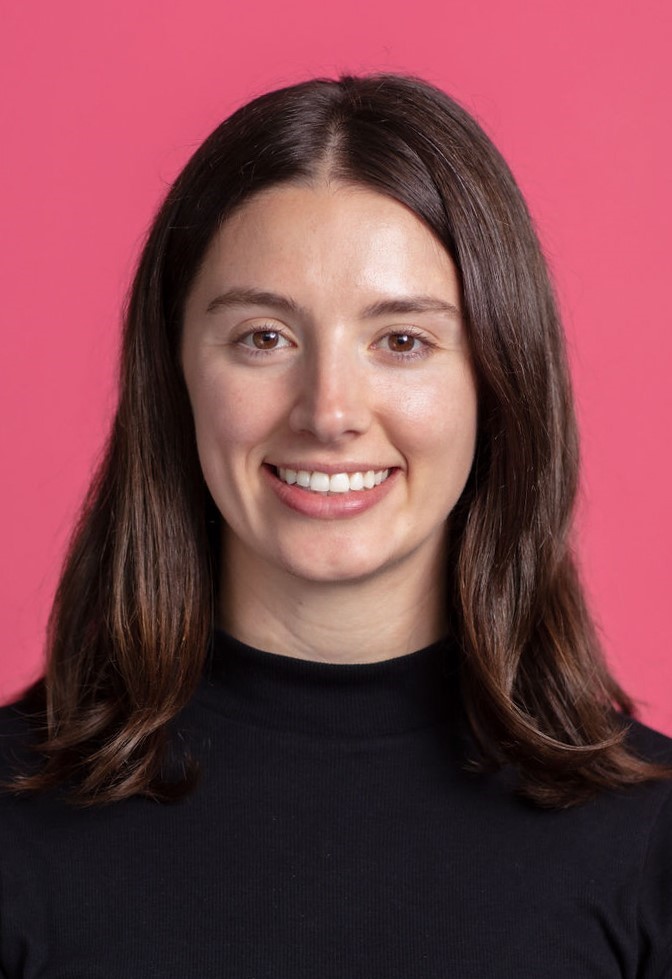 A woman smiling in front of a pink background.